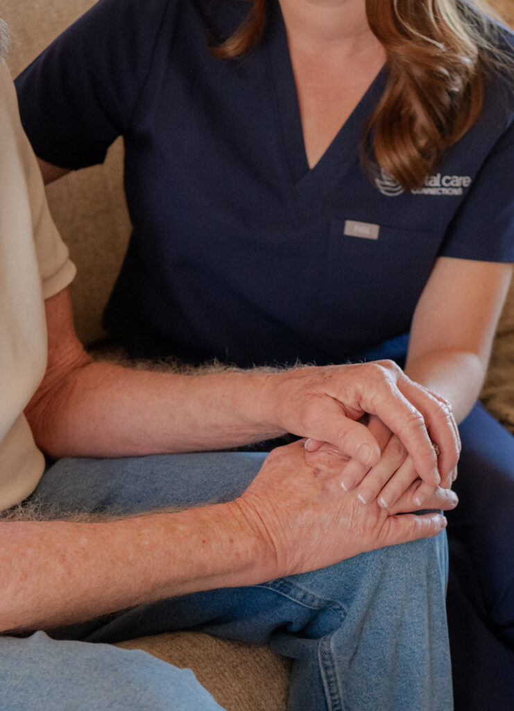 Caregiver comforting senior client, holding hands.