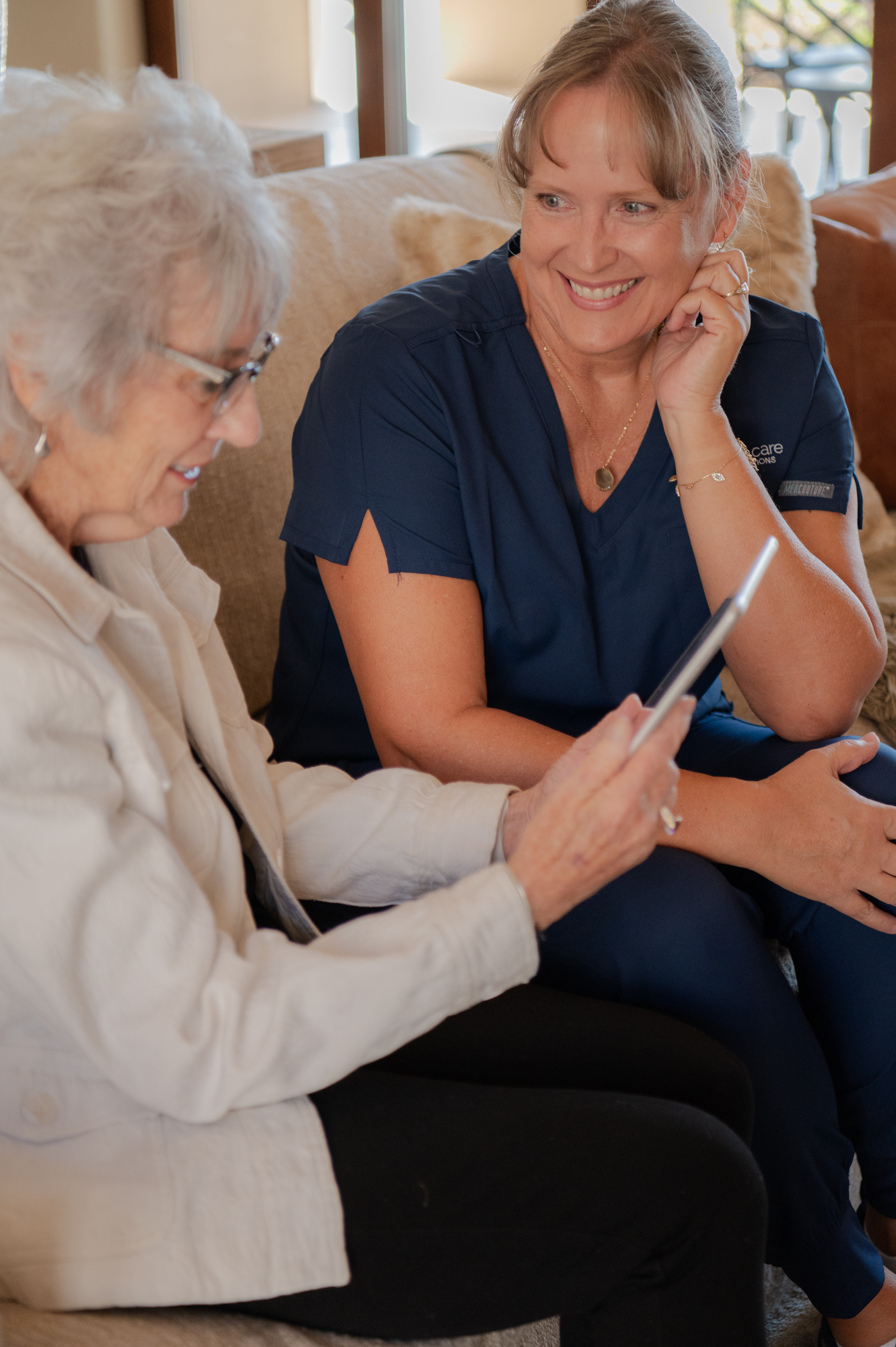 Caregiver sitting with senior client, bonding over a tablet for entertainment. Title: Caregiver and Client Bonding Over Tablet Entertainment